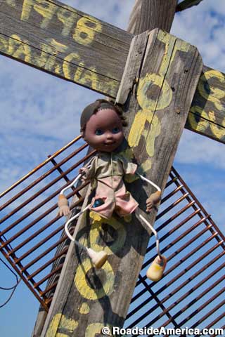 Outdoor African-American doll nailed to a weathered cross.