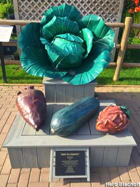 Large, full-color sculptures of a head of cabbage, a turnip, and other vegetables on an outdoor display base.