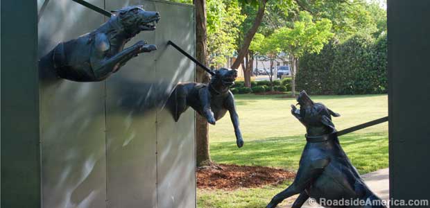 Snarling metal dogs, ready to attack, strain against leashes as they lean into both sides of a walking path.