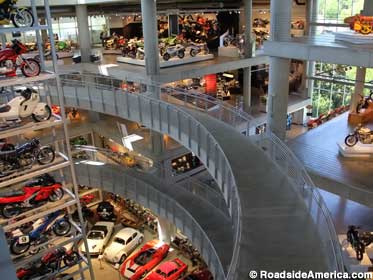 Indoor open space with ramps leading to different floors of cars and motorcycles on display.