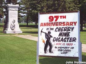 Sign notes anniversary of the Cherry Mine Disaster with monument in background.