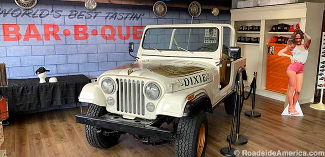 Daisy Duke tableau: Boar's Nest bar-b-que sign, Dixie jeep, and cardboard Daisy.