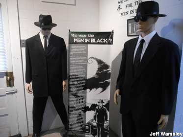 Two dummies wearing black suits, hats, and sunglasses, identified as 