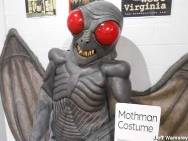 Mothman costume stands upright, with a gray body and wings, pointy teeth, and bulging red eyes.