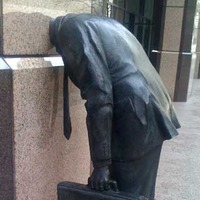 Statue of Businessman With Head Stuck In Building