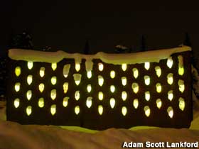 Outdoor wall embedded with clear faces that glow from within at night.