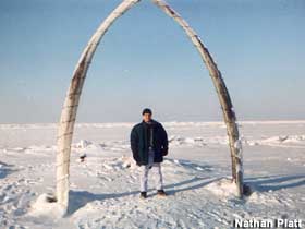 Tourist stands on a snowy landscape between two whale ribs mounted in an upright arch.