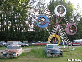 Old, rusty cars are parked around a small Ferris wheel.