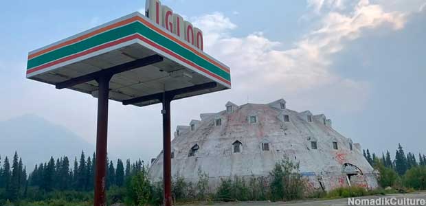 Large, white, igloo-shaped building visible behind an abandoned service station canopy.