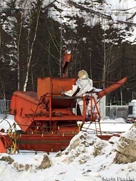 Ragged astronaut dummy sits on a red combine in the snow.