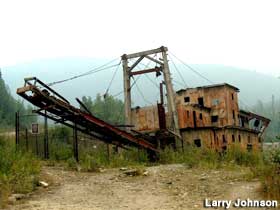 Abandoned gold dredge sits next to a road.