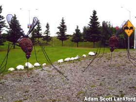 Large mosquito sculpture stands on the ground next to a highway sign.