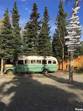 Old bus next to trees and tall signpost listing distances to nearest towns.
