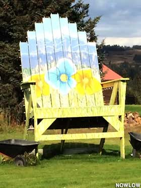 Large wooden chair painted with a yellow seat, large flowers, and a blue mountain back.