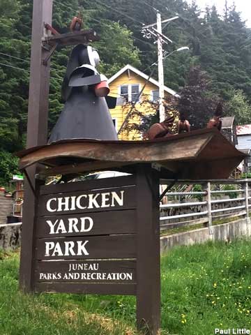 Sign for Chicken Yard Park is topped with a metal sculpture of a nun feeding chickens.
