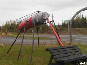 Large outdoor mosquito sculpture posed behind a bench, ready to suck blood.
