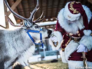 Santa bends down to hand feed one of his reindeer.