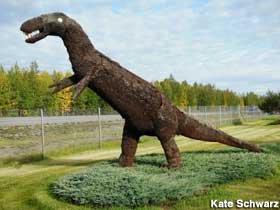 Home-made brown carnivorous dinosaur stands upright next to a highway.