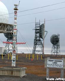 Totem pole stands among military radar dishes and microwave towers.