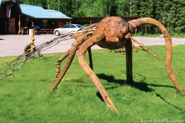 Wood sculpture or a giant mosquito next to a parking lot.