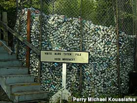 Tall poles connected by chain-link fencing enclose a large pile of discarded beer cans.