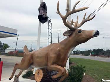 Fiberglass, full-color statue of a deer with antlers jumping over a log.