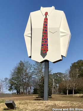 Metal sign replica of a giant white shirt with a red necktie perched atop a pole as if being worn by an invisible man.