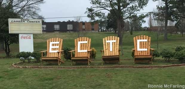 Four large outdoor chairs side-by-side with the letters ECTC on their backs, next to a sign for the Eden Career Center.