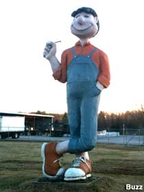 Cartoony full-color giant boy statue wears overalls and big sneakers, also has a big nose and smile.