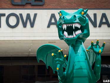 Outdoor green dragon with white teeth, yellow eyes and talons, in front of a building.