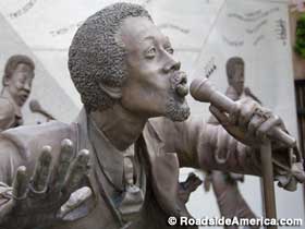 Bronze statue of Eddie Kendricks sings into a stage-mounted microphone.