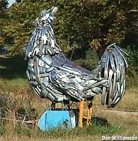 A large, outdoor sculpture of a rooster made with chrome car bumpers.