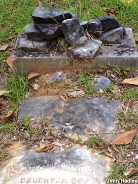 Outdoor grave with a blackened tombstone blasted into rubble by a lightning bolt.