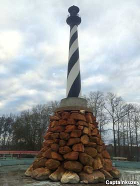 Miniature striped lighthouse replica stands atop an outdoor pile of brown rocks.