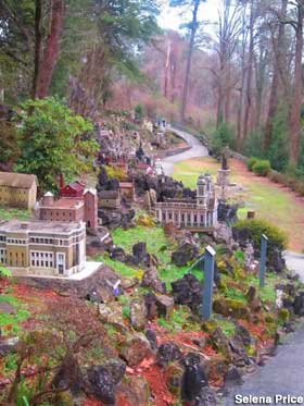 Miniature models of Mediterranean-style buildings and temples line one side of an outdoor path.