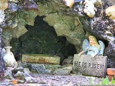 Miniature outdoor model of the tomb of Jesus has a miniature angel holding a sign, 