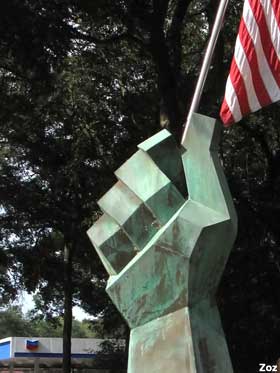 Large, greenish metal fist juts out of the ground, holding a real American flag.