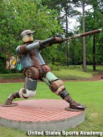 Outdoor sculpture of a baseball player swinging a bat, made of metal junk.
