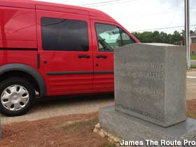 Red SUV parked next to small outdoor monument inscribed, 