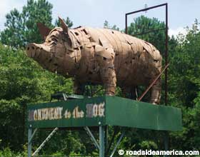 Outdoor statue of a pig made of metal junk stands on a platform, 