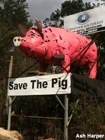 Outdoor statue of a pig made of metal junk stands on a platform with a banner, 