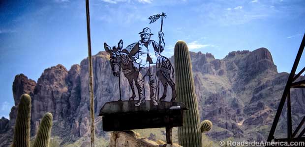 Prospector character cutout against the Superstition Mountains.