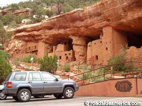 Cliff dwellings adjacent to SUV in parking lot.