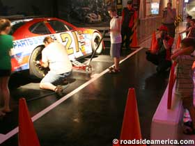 Tourists in a simulated pit race a clock to change a tire.