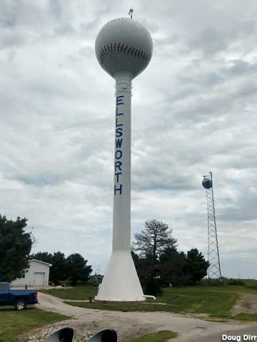 Municipal water tower with town name painted on the lower stem and a baseball on top.
