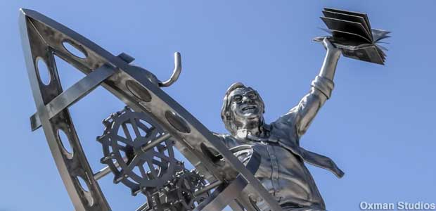 Steel sculpture of Ray Bradbury astride a rocket silhouetted against blue sky.
