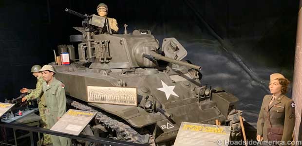 An indoor display features a World War II tank with mannequins of soldiers .