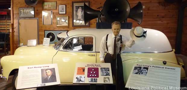 Mannequin of Earl Long in shirt sleeves, standing in front of an old car with giant loudspeakers on its roof.