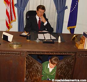 John John Kennedy futilely hides under his fathers desk, hoping the Conspiracy won't find him.