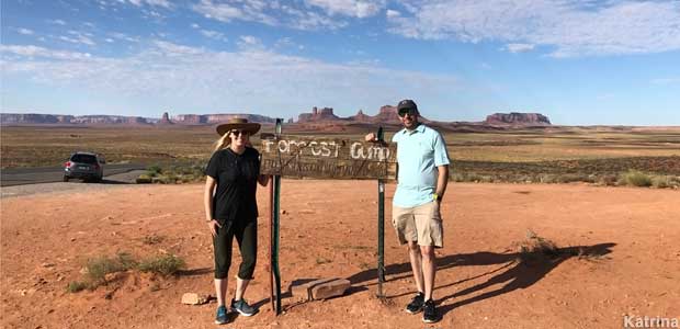 Two travelers pose with Forrest Gump sign on picturesque western landscape.